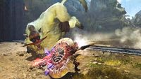 A warrior in dark armor blocks a leaping, furry, tusked monster with a large, glowing, circular shield in a rocky, dusty outdoor environment.