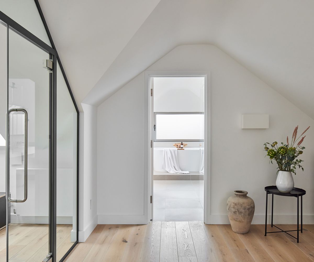 An open door leading to a large en suite bathroom from a light-filled bedroom