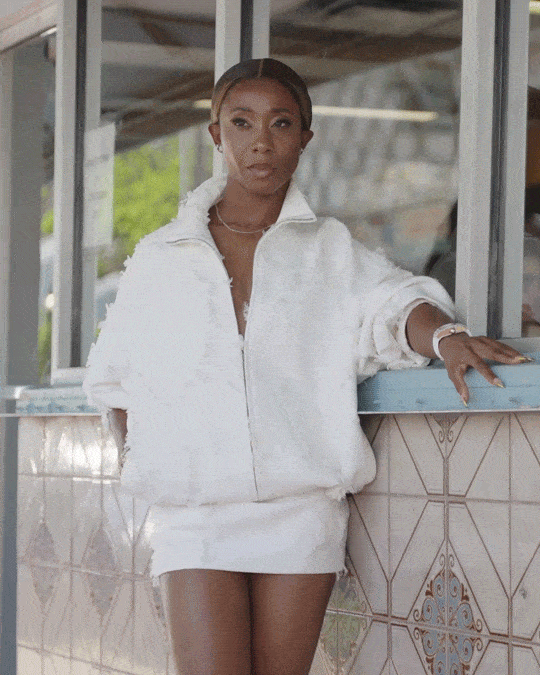 Shelly Ann Fraser Pryce wearing a white skirt and white hooded sweater standing outside a storefront