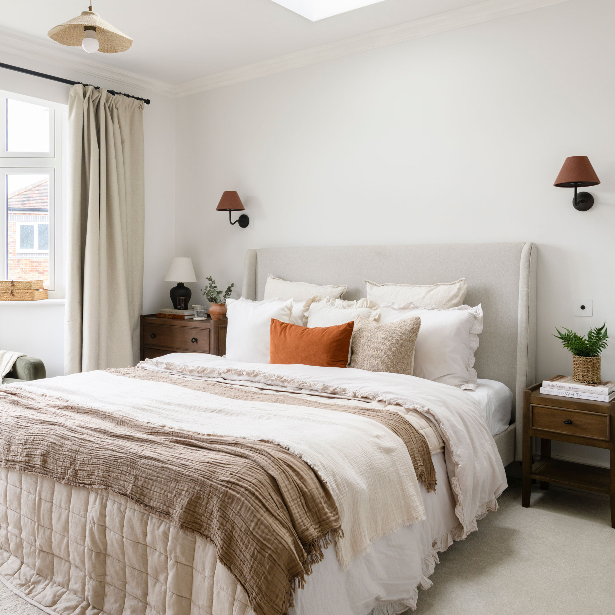 White bedroom with neutral fabric headboard and wall lights