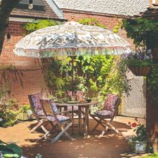 A patio with a folding wooden outdoor dining set with a round table and four chairs and a patterned parasol