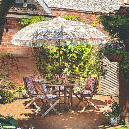 A patio with a folding wooden outdoor dining set with a round table and four chairs and a patterned parasol