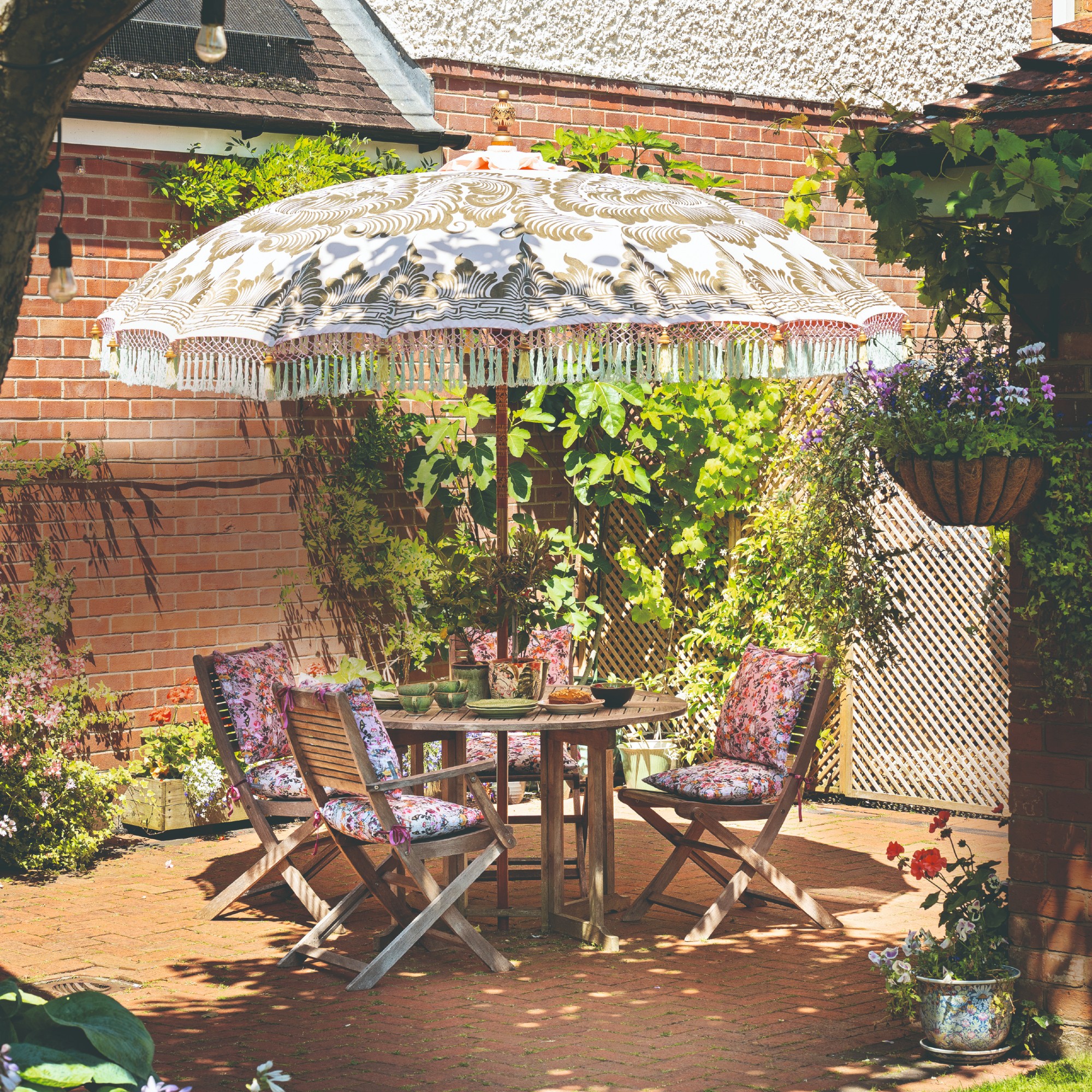 A patio with a folding wooden outdoor dining set with a round table and four chairs and a patterned parasol