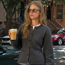 Danish style influencer and creative Clara Dyrhauge holding a coffee wearing a chic outfit with a gray fitted cardigan and dark jeans—the winter 2025 2026 dark-wash denim trend