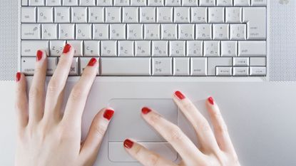 Woman wearing red nail polish, typing on laptop keyboard