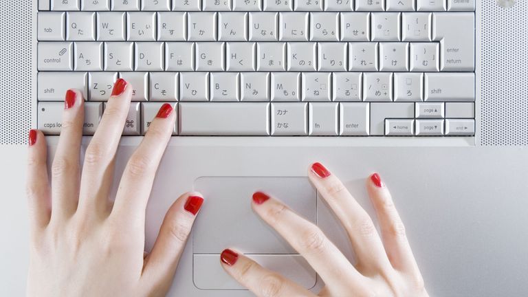 Woman wearing red nail polish, typing on laptop keyboard