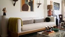 Image of a modern, white couch with striped bolster pillows and a lime throw blanket. There is a marble coffee table with books and a candelabra on it. The table beside the sofa has a pink lamp with a leopard shade.