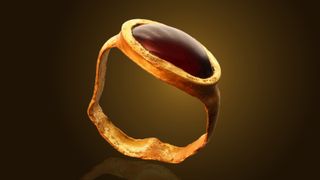 Gold ring with gemstone against spotlight on black background.
