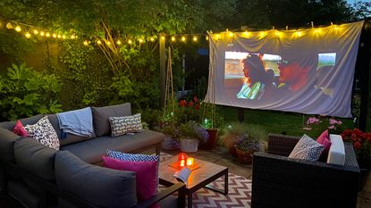 portable projector and screen in garden at night with sofa and festoon lights