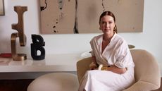 Louise Olsen of Dinosaur designs sitting on a chair with some sculptural pieces on a table alongside 