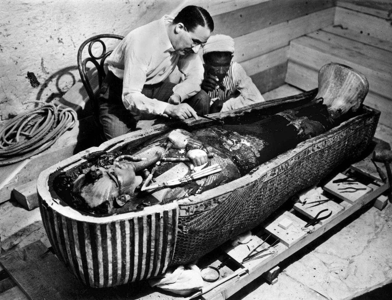 Howard Carter and an Egyptian archaeologist stand over the sarcophagus of Tutankhamun