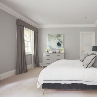 Grey walls, neutral carpet, dark grey curtains in front of window and white bed