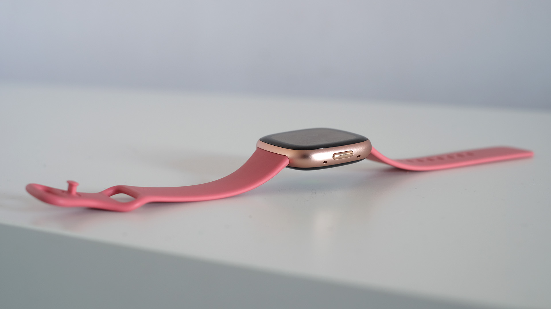 Side of the Fitbit Versa 4 with pink strap on white table