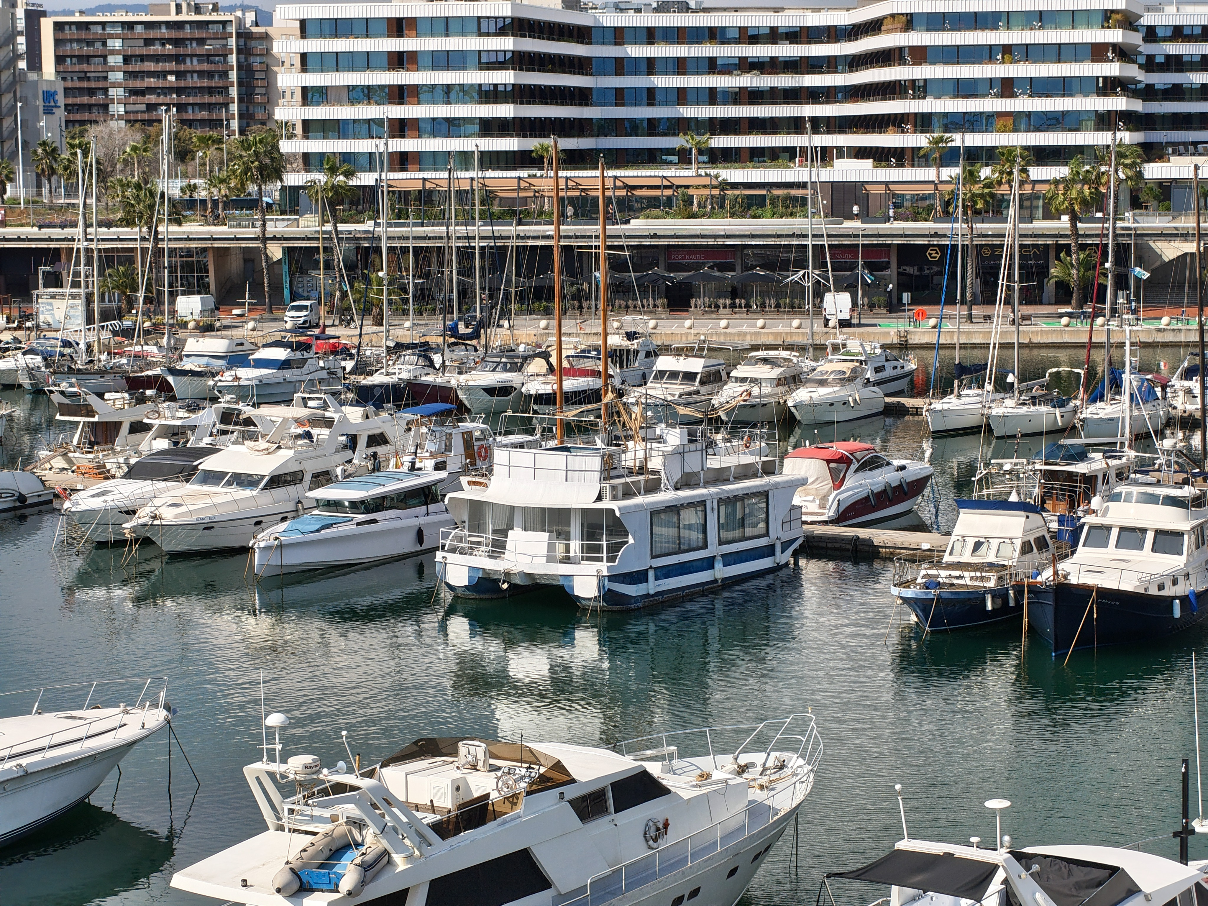 Zoomed-in shot of boats docked in a marina with a modern waterfront building behind them, captured with the Nothing Phone (4a).