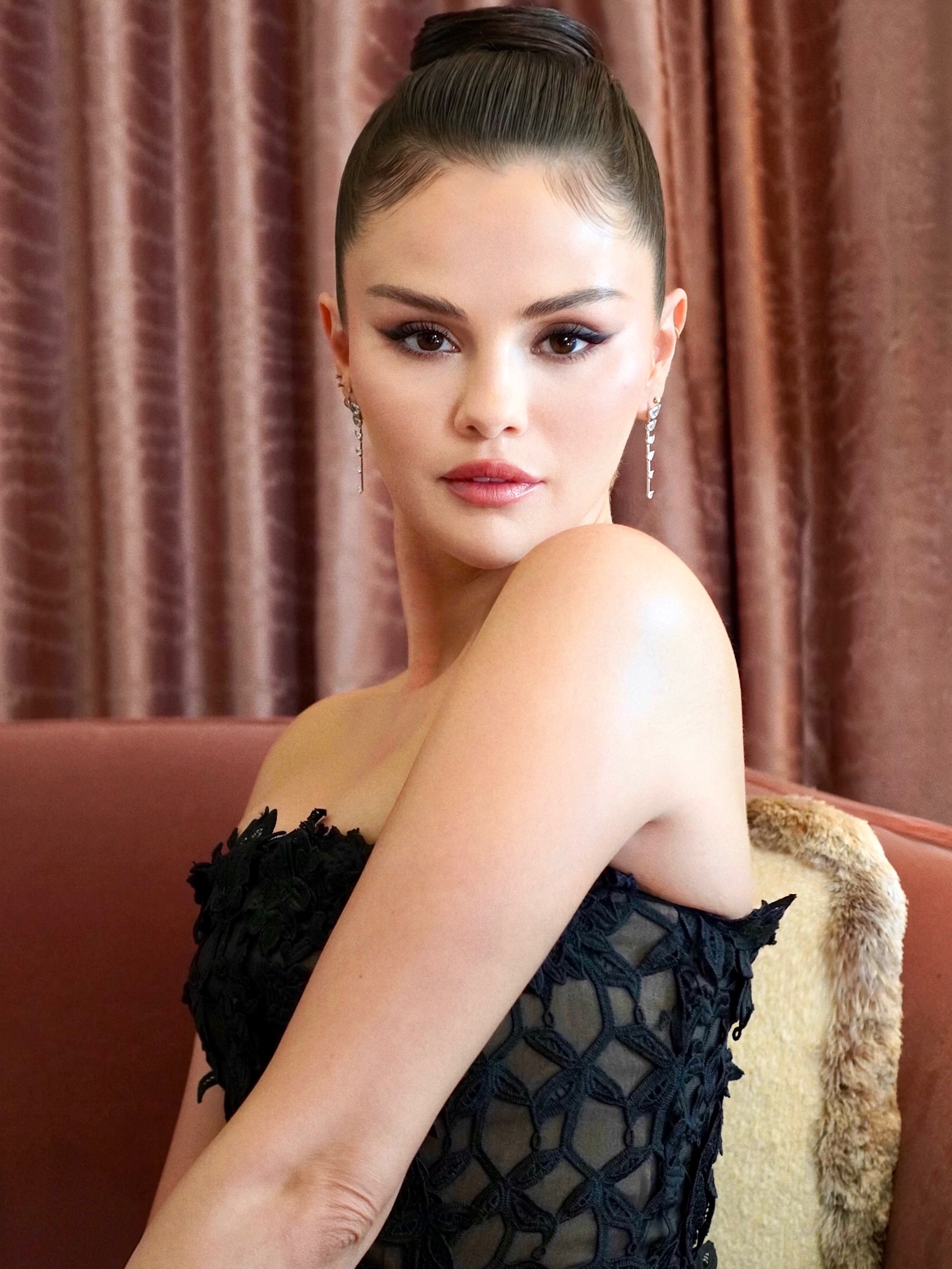 Selena Gomez poses in a strapless black dress with a subtly nude design featuring sheer panels with her hair worn in a high bun