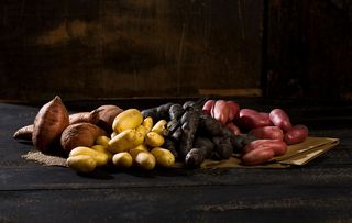 Different sorts of potatoes on brown paper, jute and dark wood