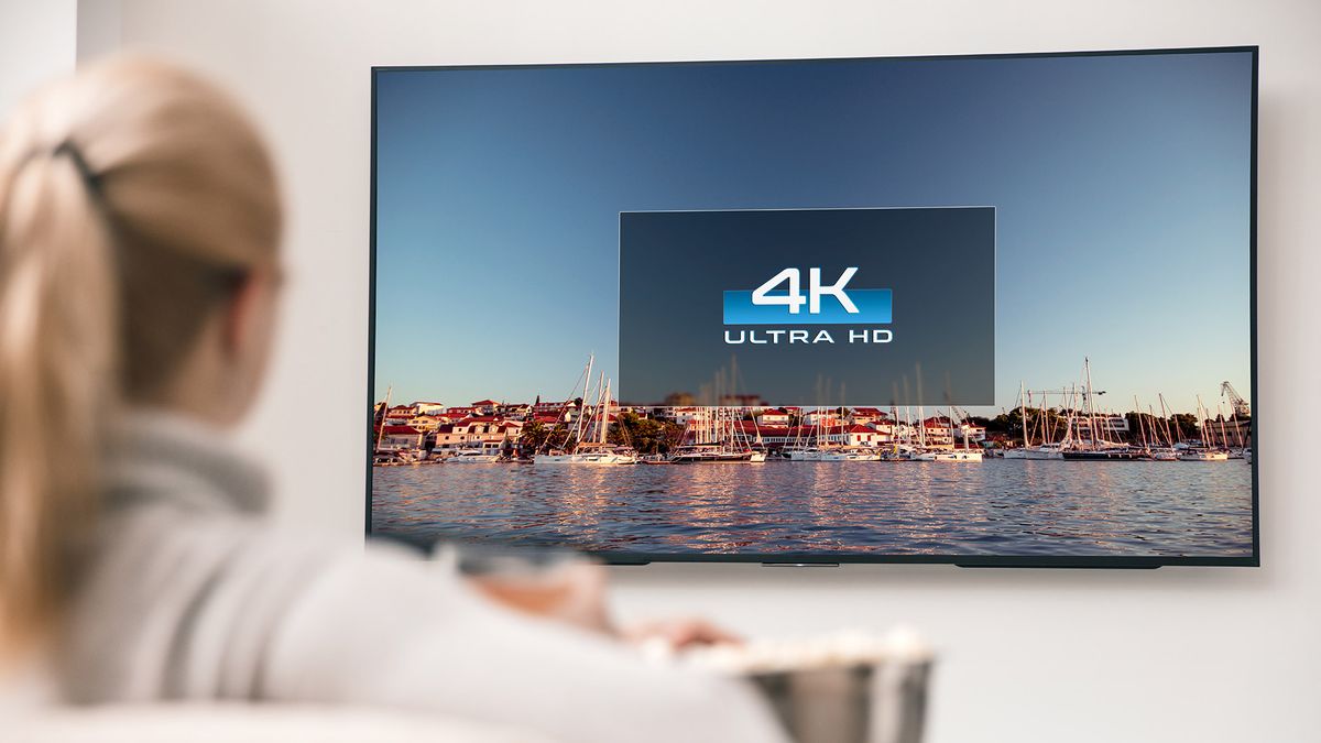 Woman sitting in front of a TV with a logo reading &#039;4K Ultra HD&#039; on the screen