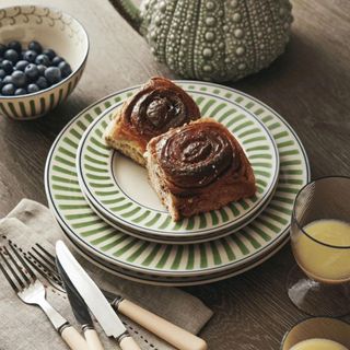 Green lined serving plates with two cinnamon rolls on top, next to some cutlery on a wooden table