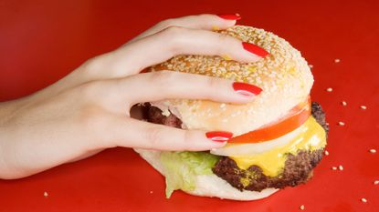 Lady's hand with red nails holding a hamburger