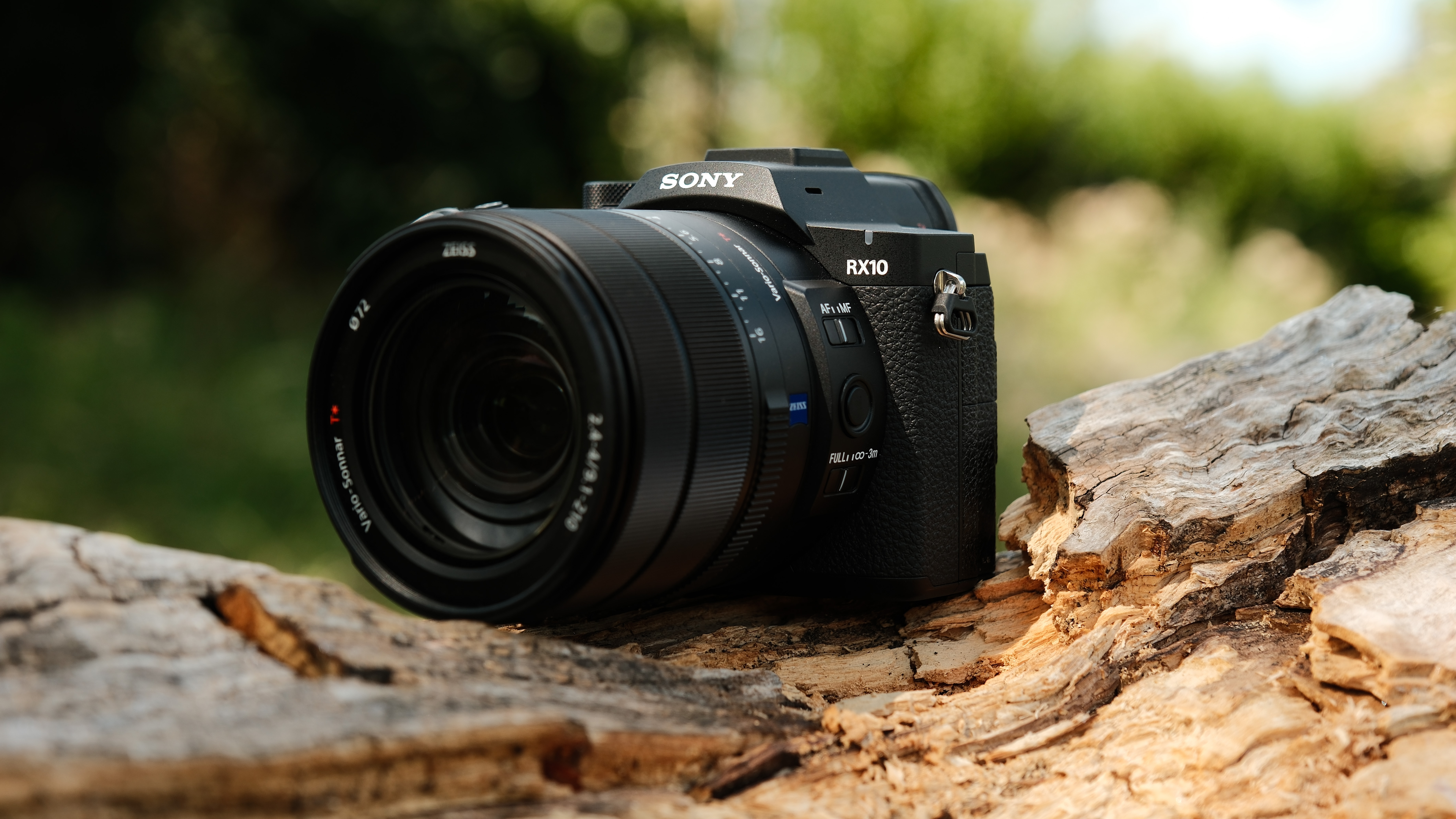 Front view of the Sony RX10 V positioned on a fallen tree trunk outdoors.