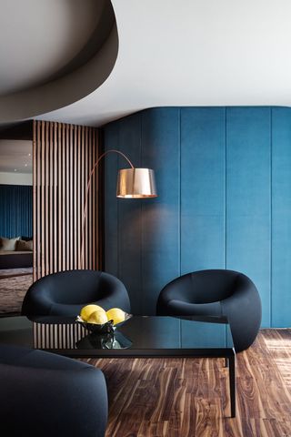 A sitting area with round leather chairs, a black coffee table, a floor lamp, blue walls and wooden floors.