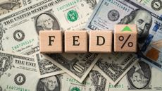 Wooden blocks spelling out FED plus a percentage sign, sitting on top of dollar bills