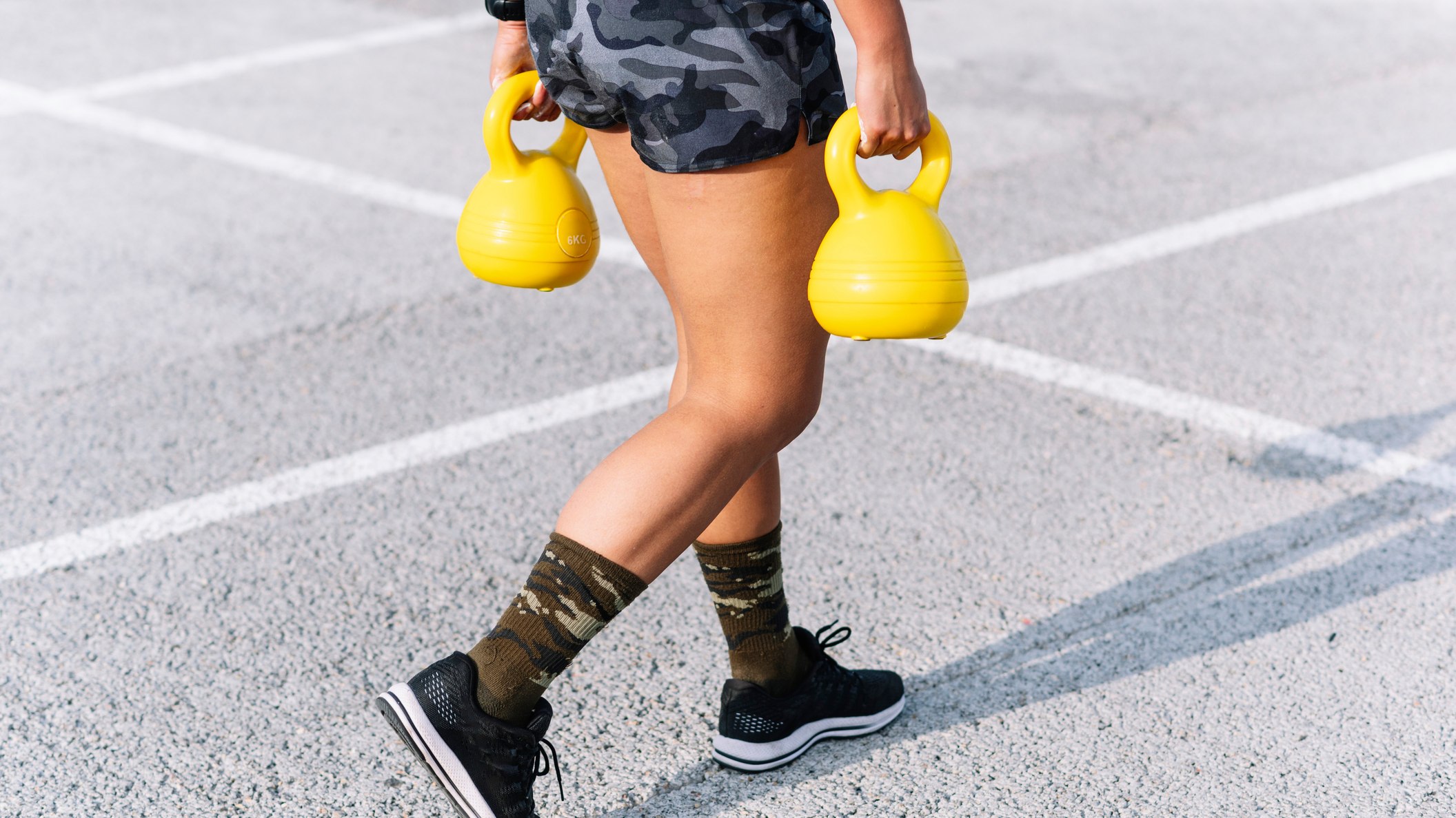 Woman carrying yellow kettlebells in a farmer's carry