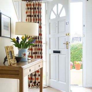White hallway, open front door, cream carpet, wooden sidetable