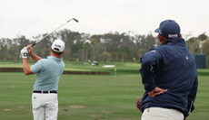 Bud Cauley hits a shot on the range while his coach stands behind him