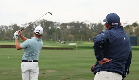 Bud Cauley hits a shot on the range while his coach stands behind him