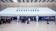 Terminal 2 departures building at Manchester Airport, run by Manchester Airports Group, with passengers queuing at check-in point.