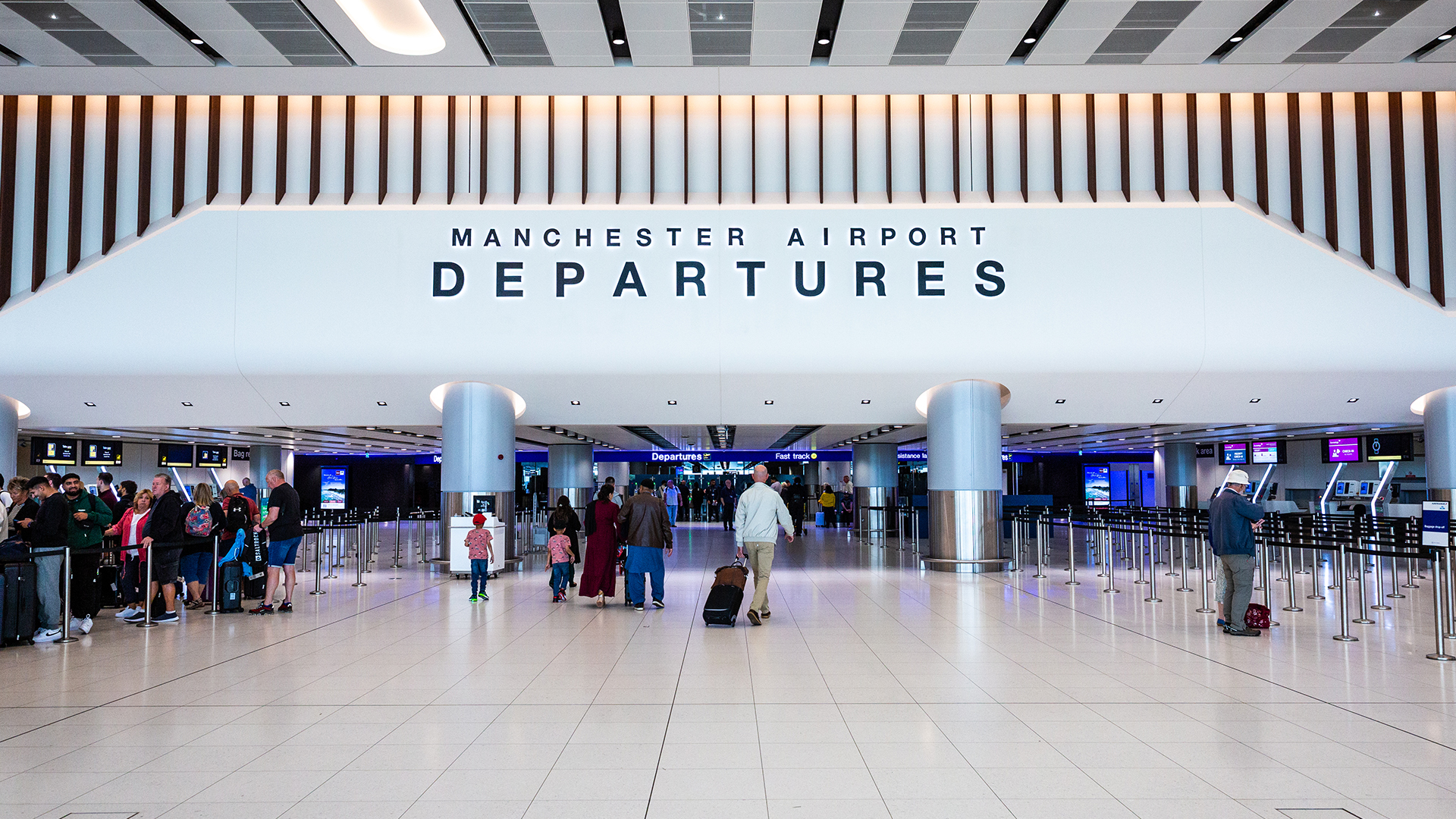 Terminal 2 departures building at Manchester Airport, run by Manchester Airports Group, with passengers queuing at check-in point.