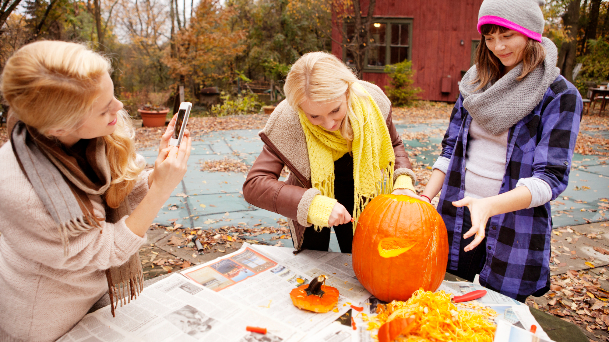 Two women carving a pumpkin for Halloween, with somebody else taking a photo of them.