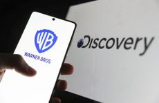 The Warner Bros. logo on a smartphone with the Discovery logo on a laptop in the background