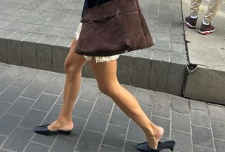 Annelaure Mais wearing a white miniskirt with black heeled mules and carrying a brown suede tote bag.