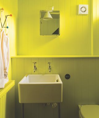 Bright yellow color drenched bathroom, shiplap, small mirror, square basin, towel hooks,