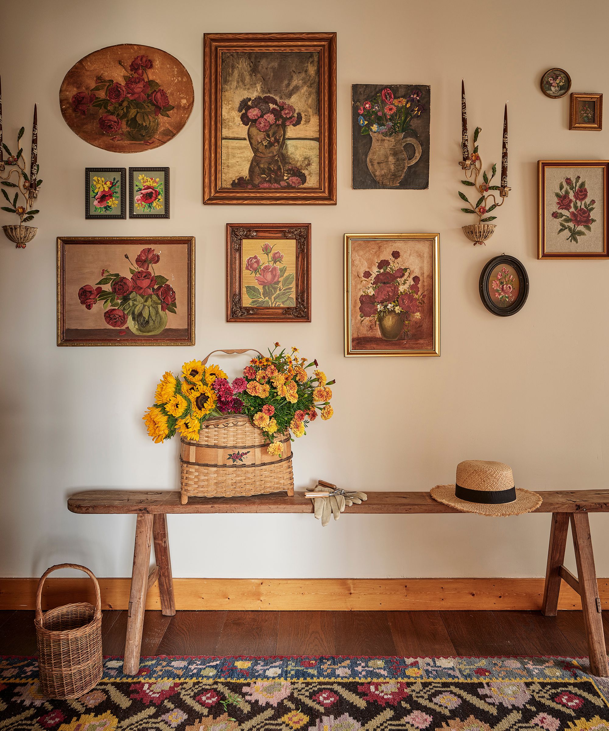 a vintage style hallway with a rustic wooden bench, a galley wall of floral vintage paintings and a folk rug