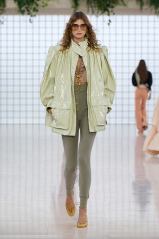 a Chloé model wears green leggings, yellow shoes, pink top, and a green leather jacket.