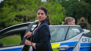 Natalie Dew as DS Tanika Malik stands by a police car in The Marlow Murder Club.