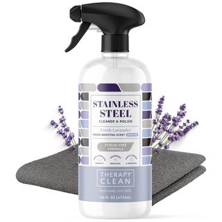 A white bottle of stainless steel cleaner with purple label, black spray lid, grey towel and lavender