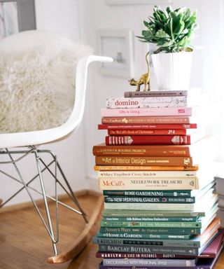 A living room with white chair and stack of hardback books in rainbow order
