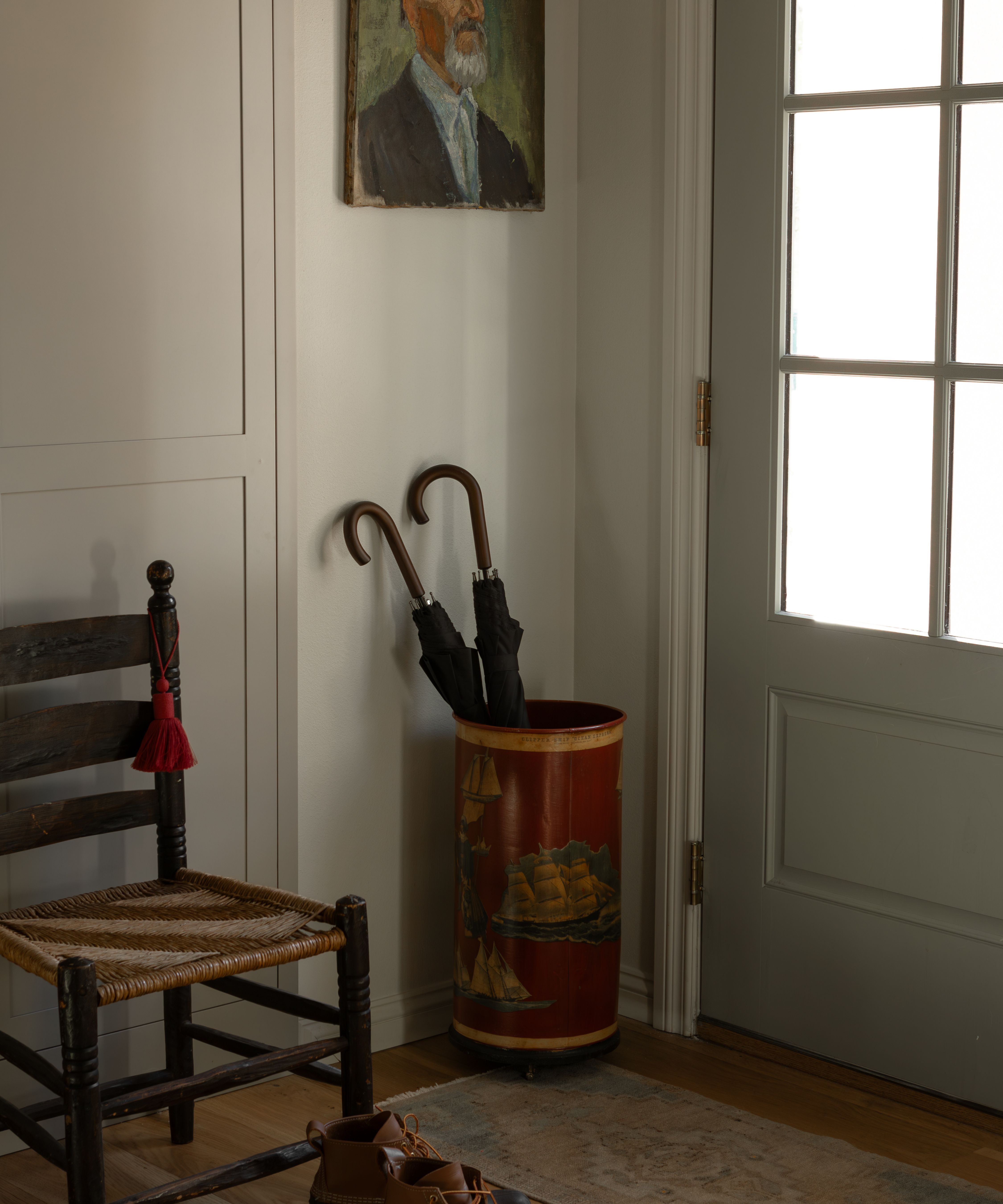 a small entryway of a carriage house with a sage green front door, antique umbrella stand, a vintage painting of a man with a vintage wooden chair