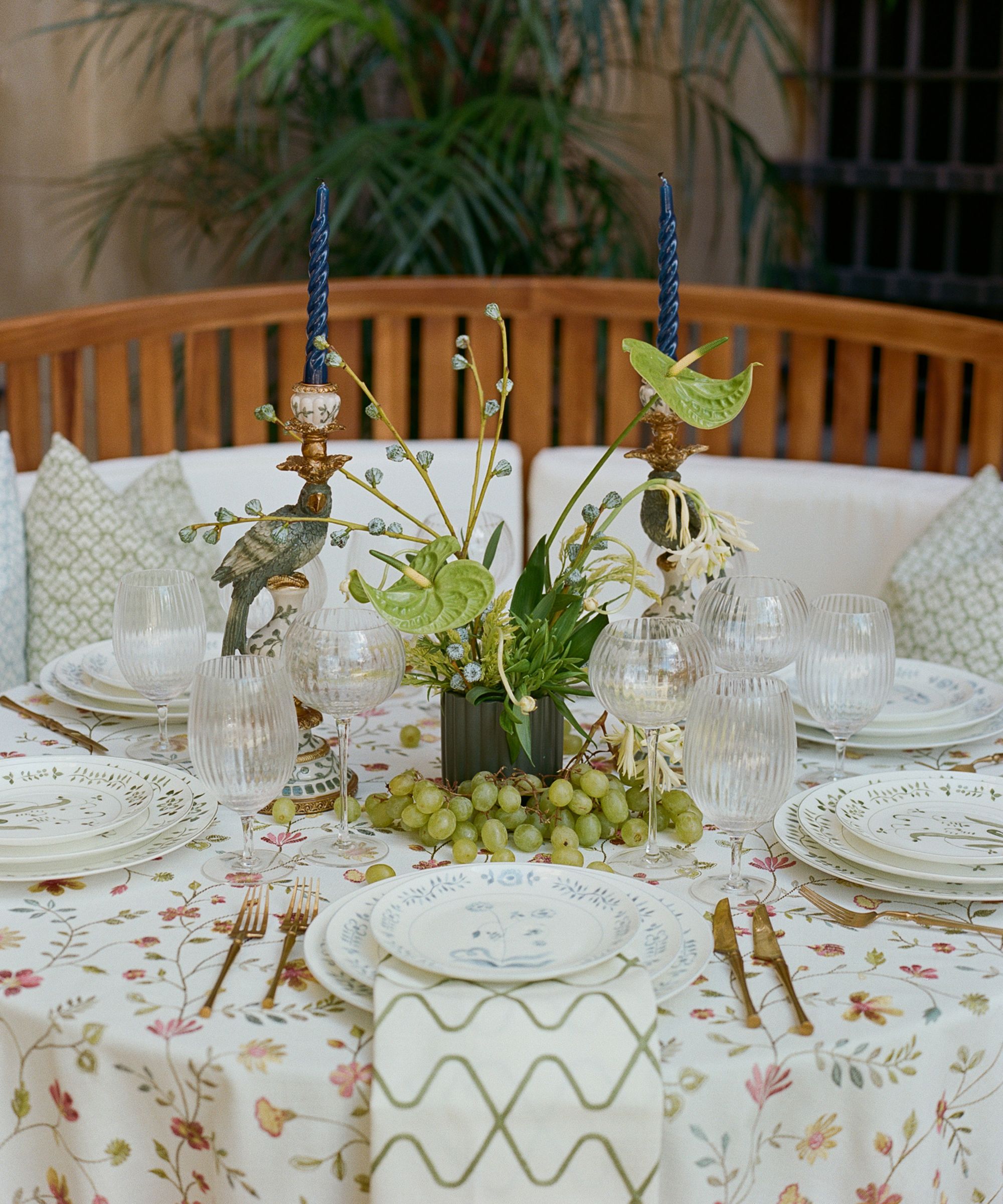 Outdoor tablescape with layered linens and glassware and a green floral centerpiece with green grapes