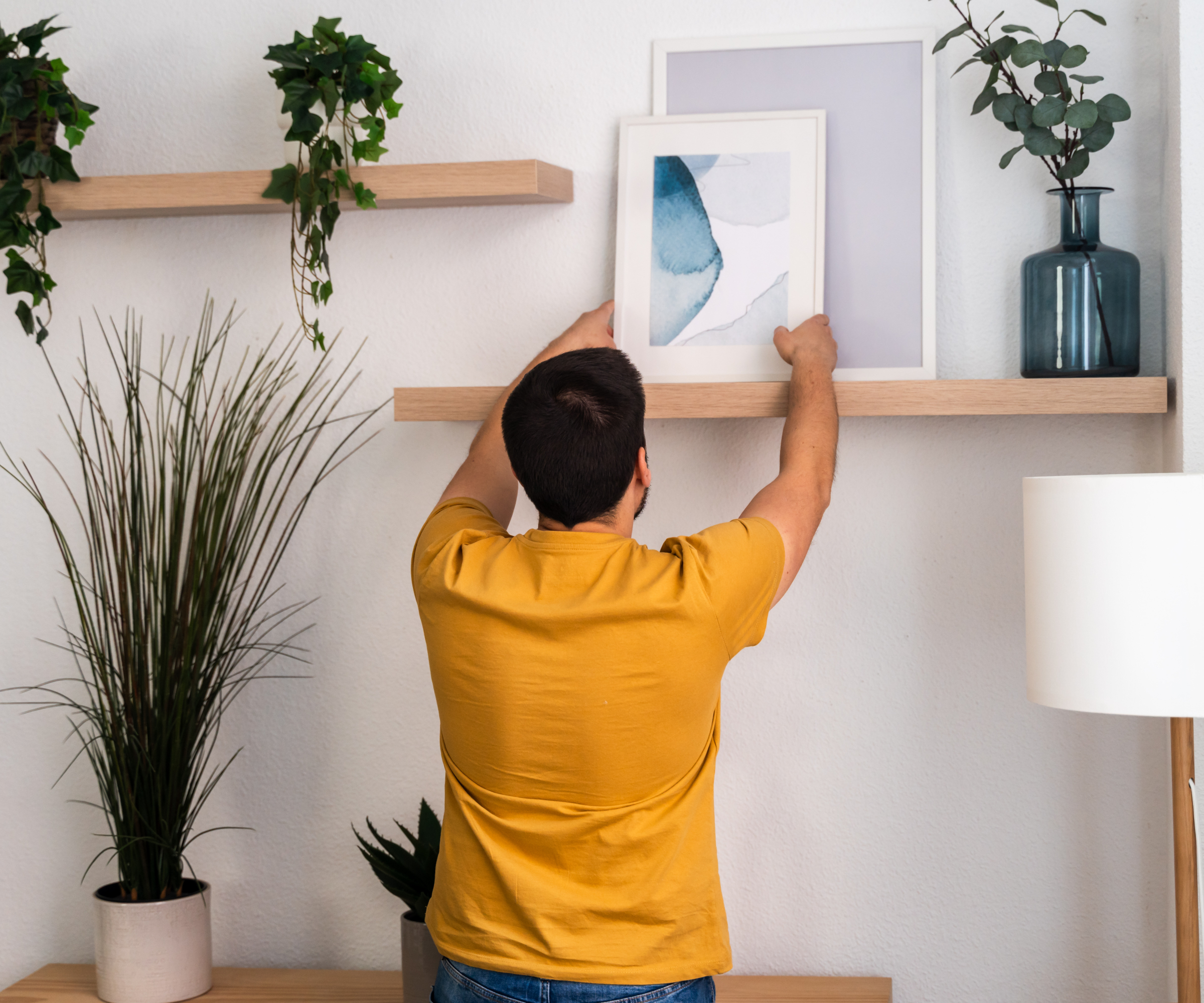 man putting artwork on wooden wall mounted shelves