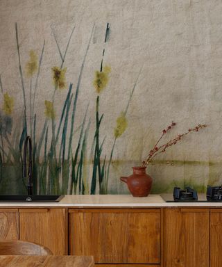 wooden kitchen units, white worktop and wallpaper with delicate flower and reed design