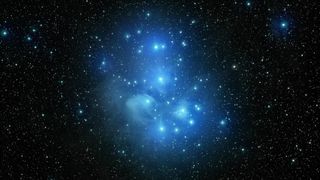 Image of Pleiades, an open star cluster (also known as the Seven Sisters and Messier 45). There are a number of bright stars that stand out amongst the rest, surround by a faint dust cloud.