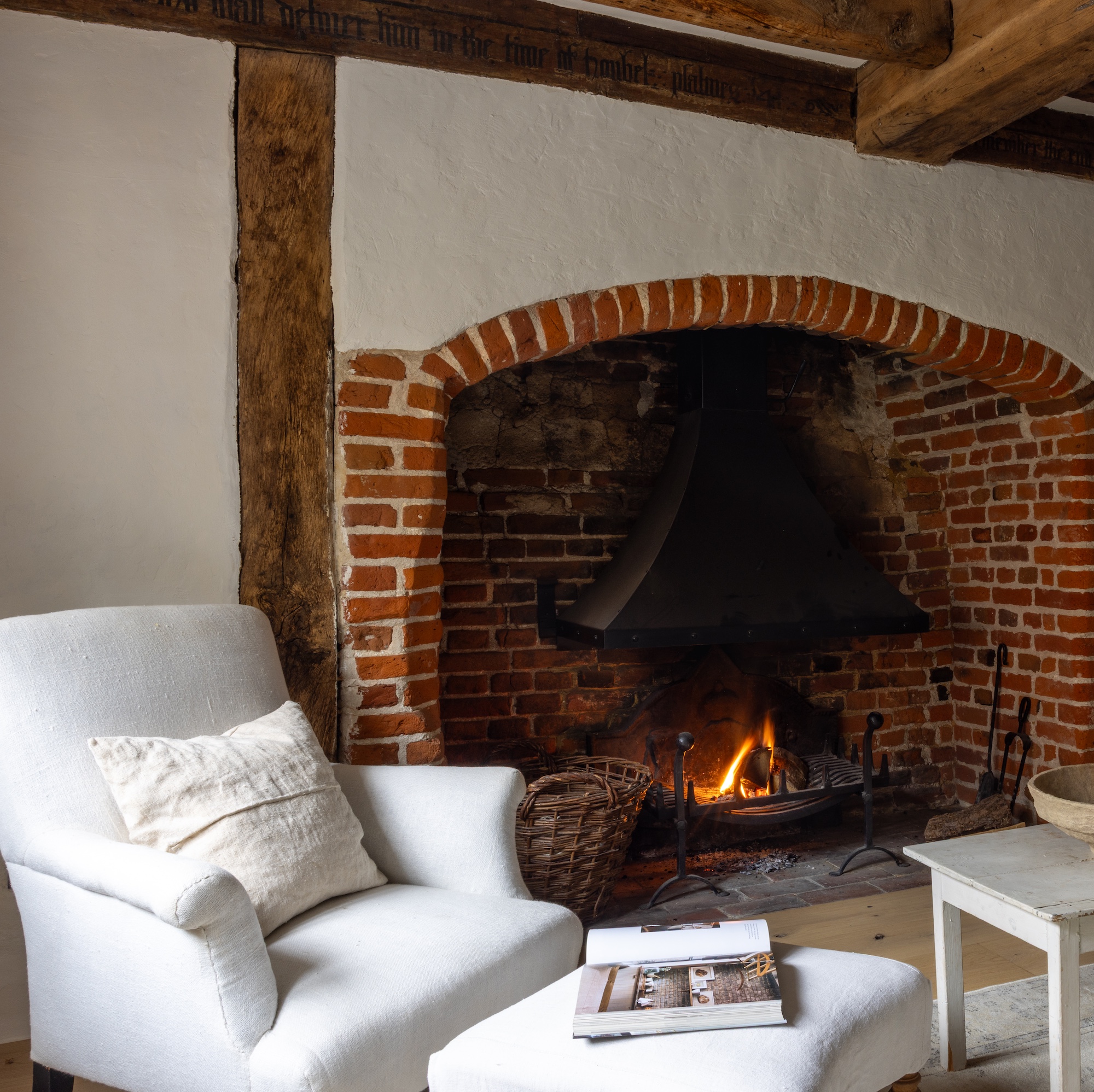 large brick inglenook fireplace in old cottage with beamed walls and ceilings and white armchair
