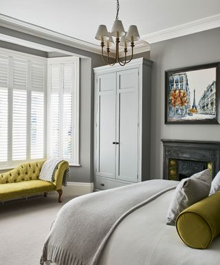 grey bedroom with chartreuse chaise longue and cushions, fireplace and shutters