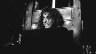 Alice Cooper performing onstage with his head in a guilotine in the 1970s