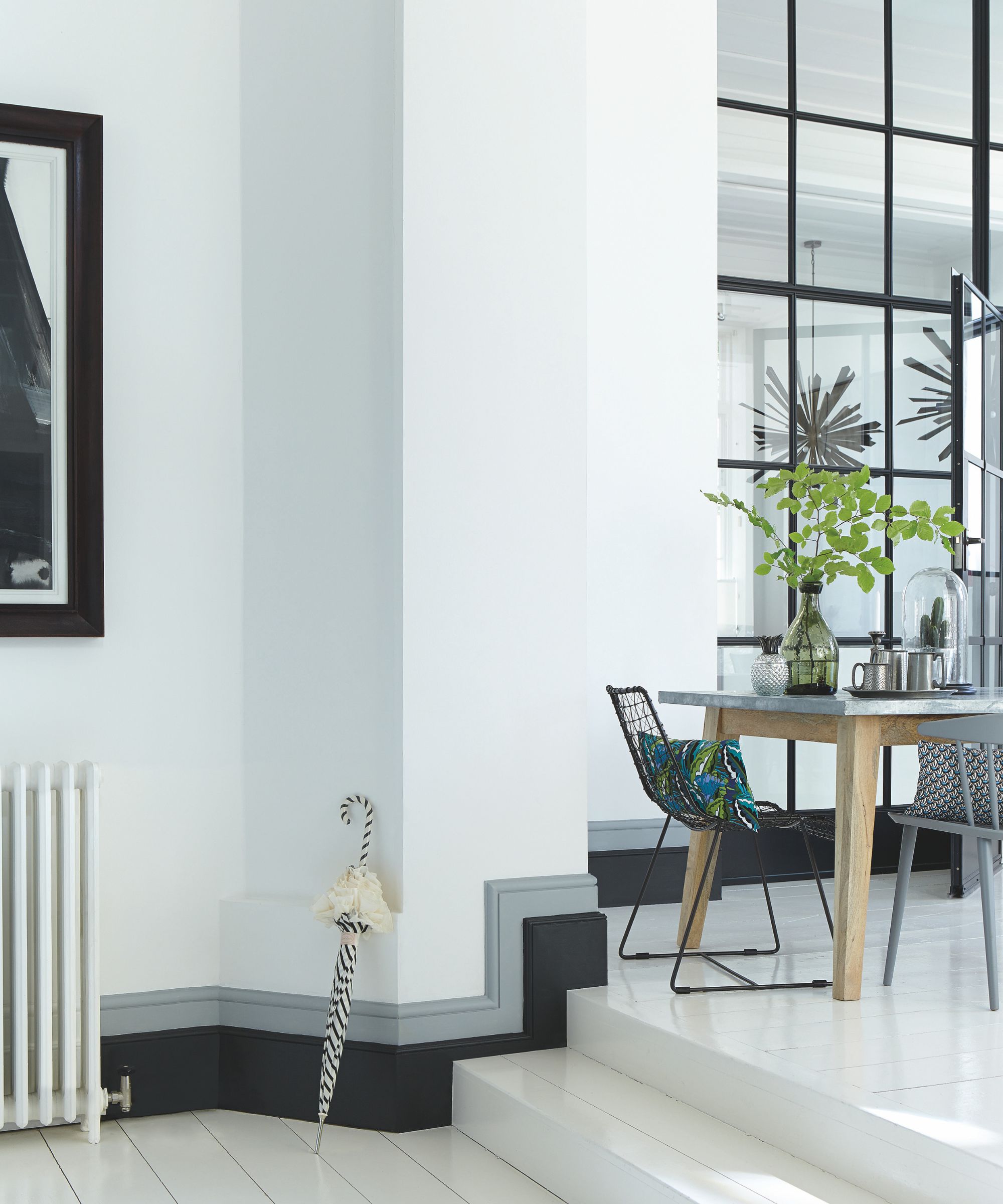 A white minimalist living space with a small table and chairs with a vase of foliage